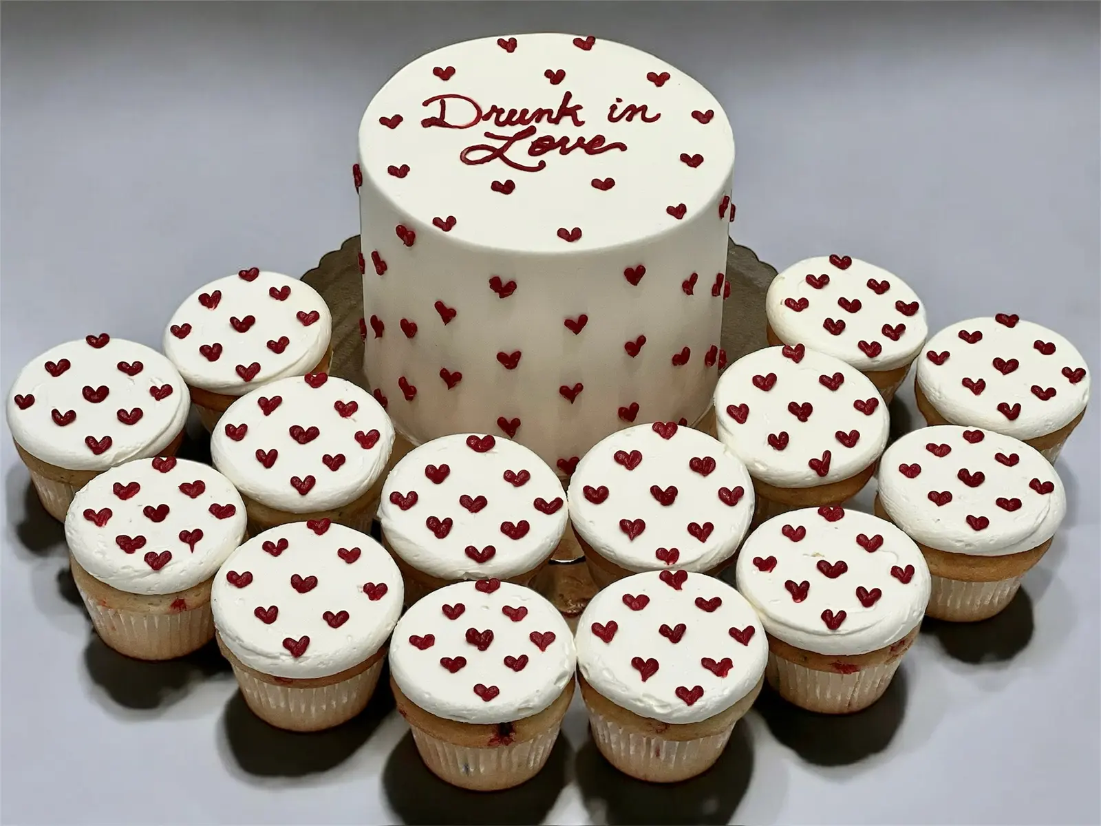 Heart-decorated cake surrounded by matching cupcakes